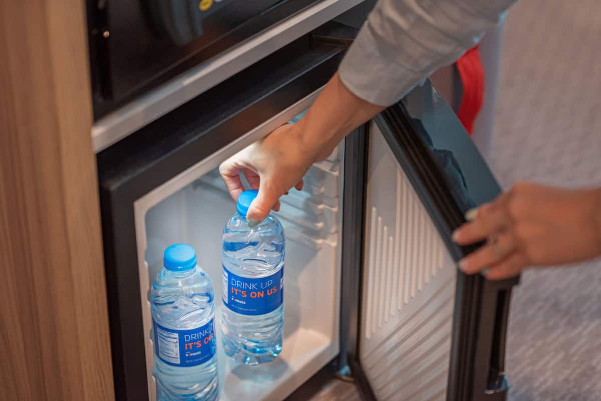 A hand reaching into a refrigerator to grab a water bottle.