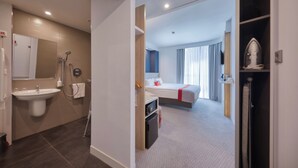 Quarto de hotel com banheiro, cama, mesa de cabeceira e guarda-roupa.