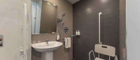 A modern bathroom with a sink, mirror, shower, and a wheelchair-accessible chair.
