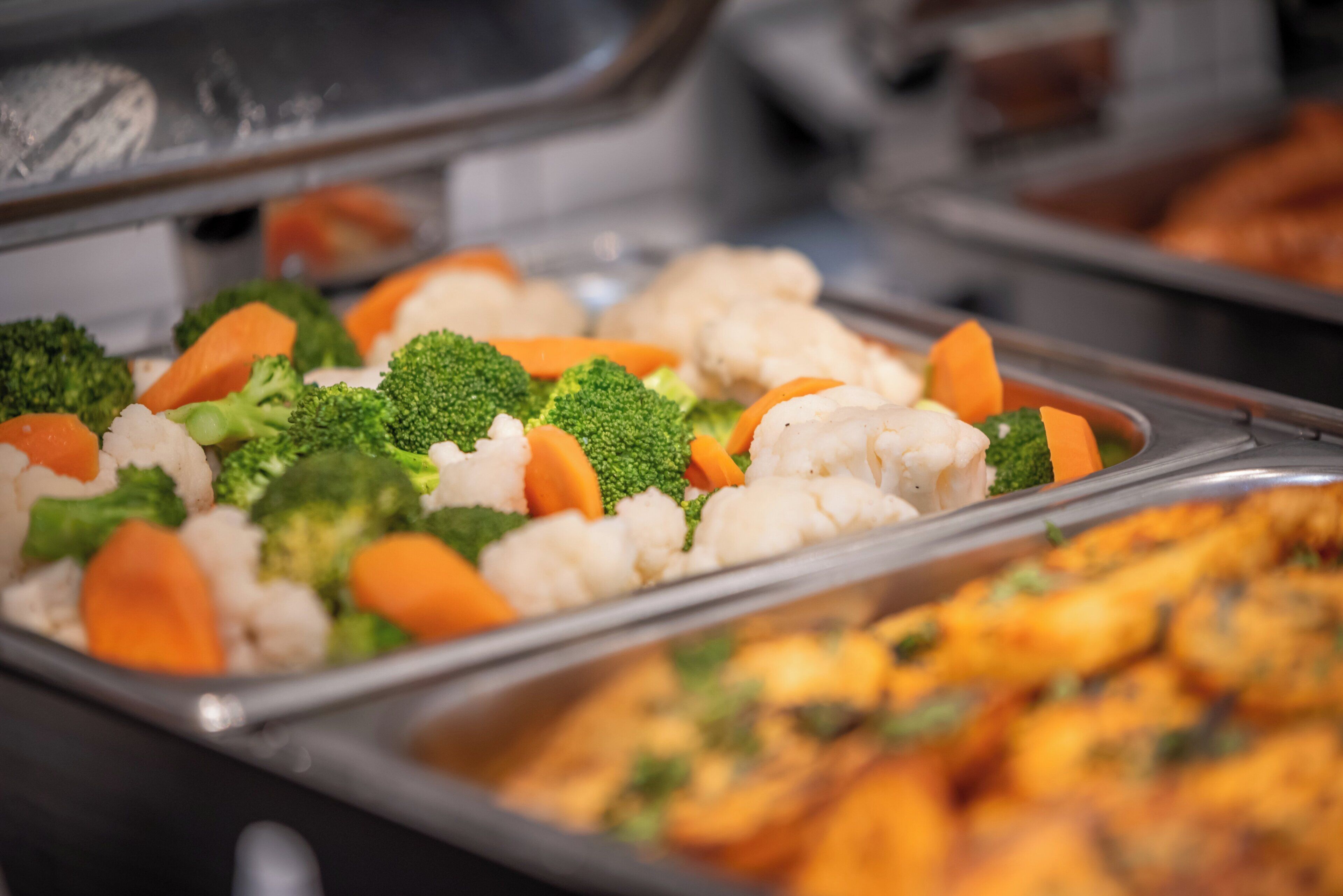 Un buffet proposant une variété de légumes, notamment des brocolis, des carottes et du chou-fleur.