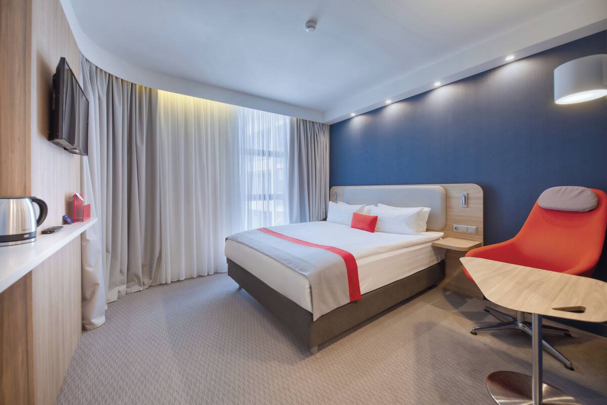 A modern hotel room with a bed, a desk, a chair, and a television.