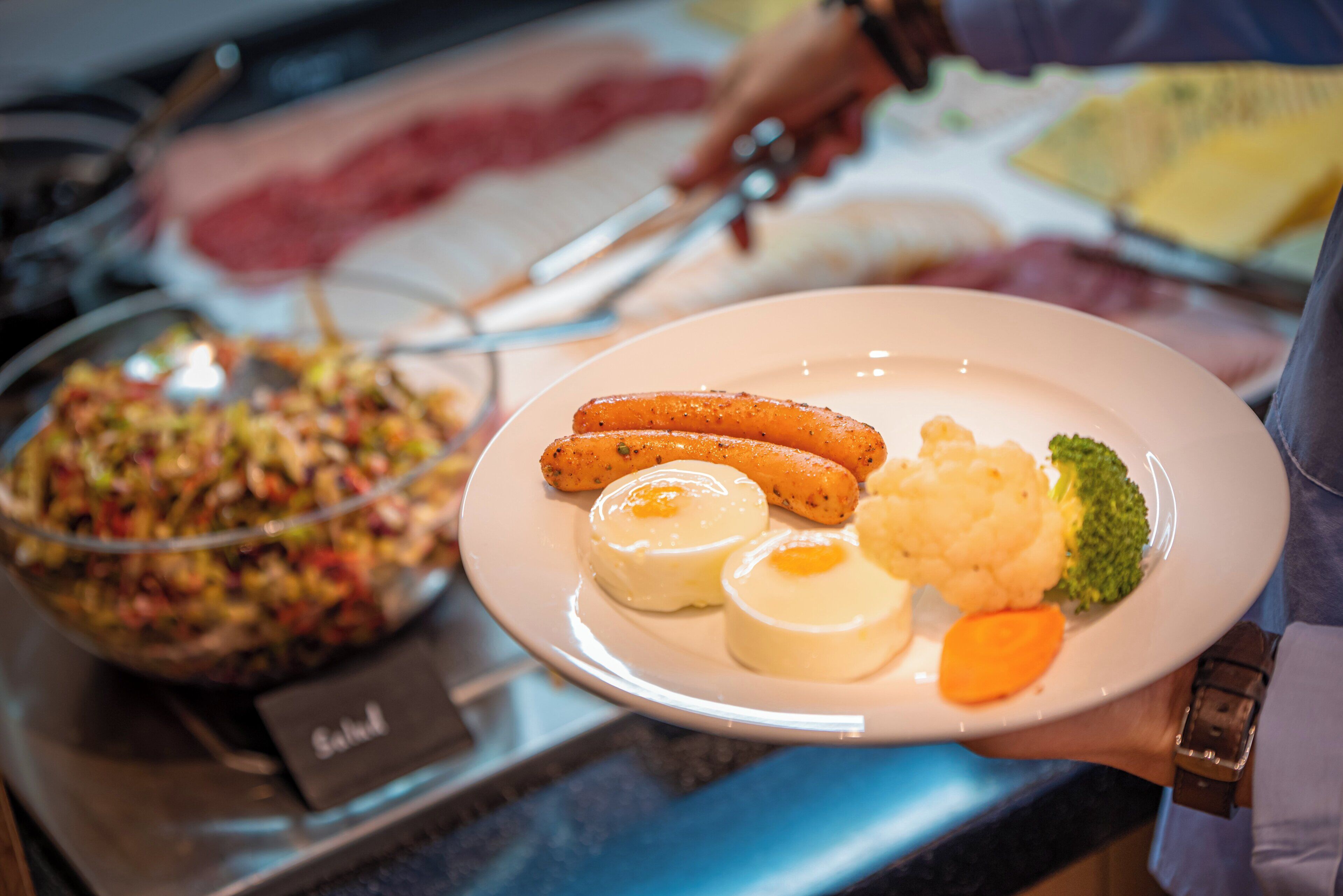 Une table de buffet proposant divers plats, notamment des saucisses, de la purée de pommes de terre et une salade.