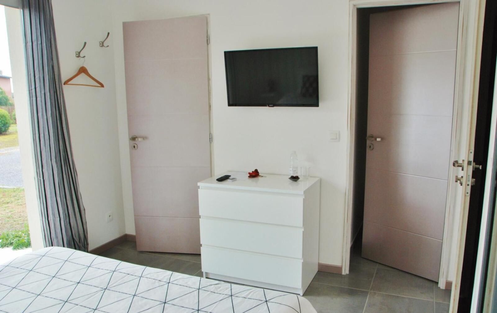 Un dormitorio con una cama, un aparador blanco, un televisor en la pared y dos puertas.