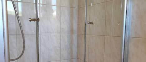Un espacio de ducha con puerta de vidrio, un cabezal de ducha de mano y un taburete pequeño con una toalla.