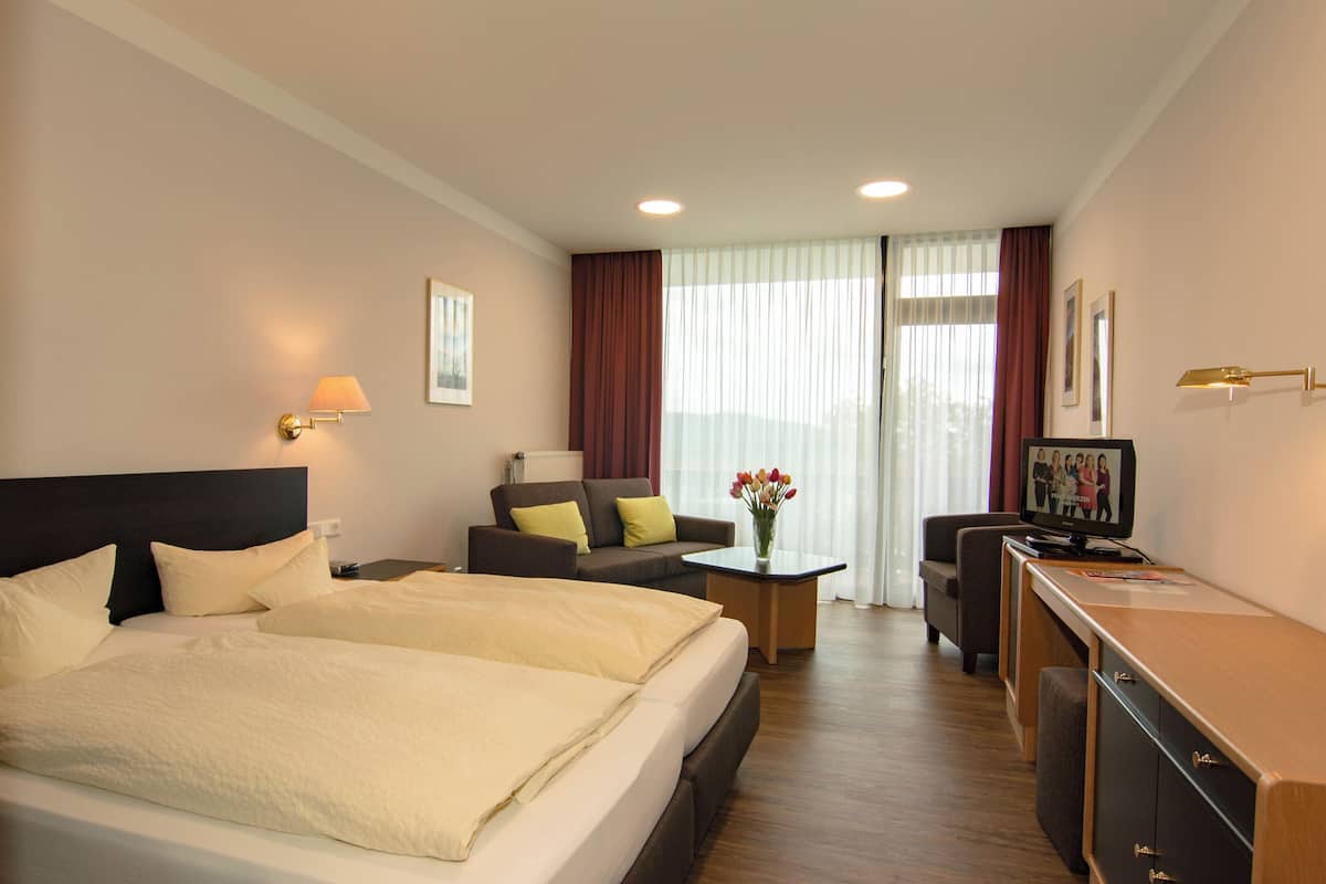Ett hotellrum med en stor säng, en soffa, ett skrivbord med en dator och ett fönster med gardiner.
