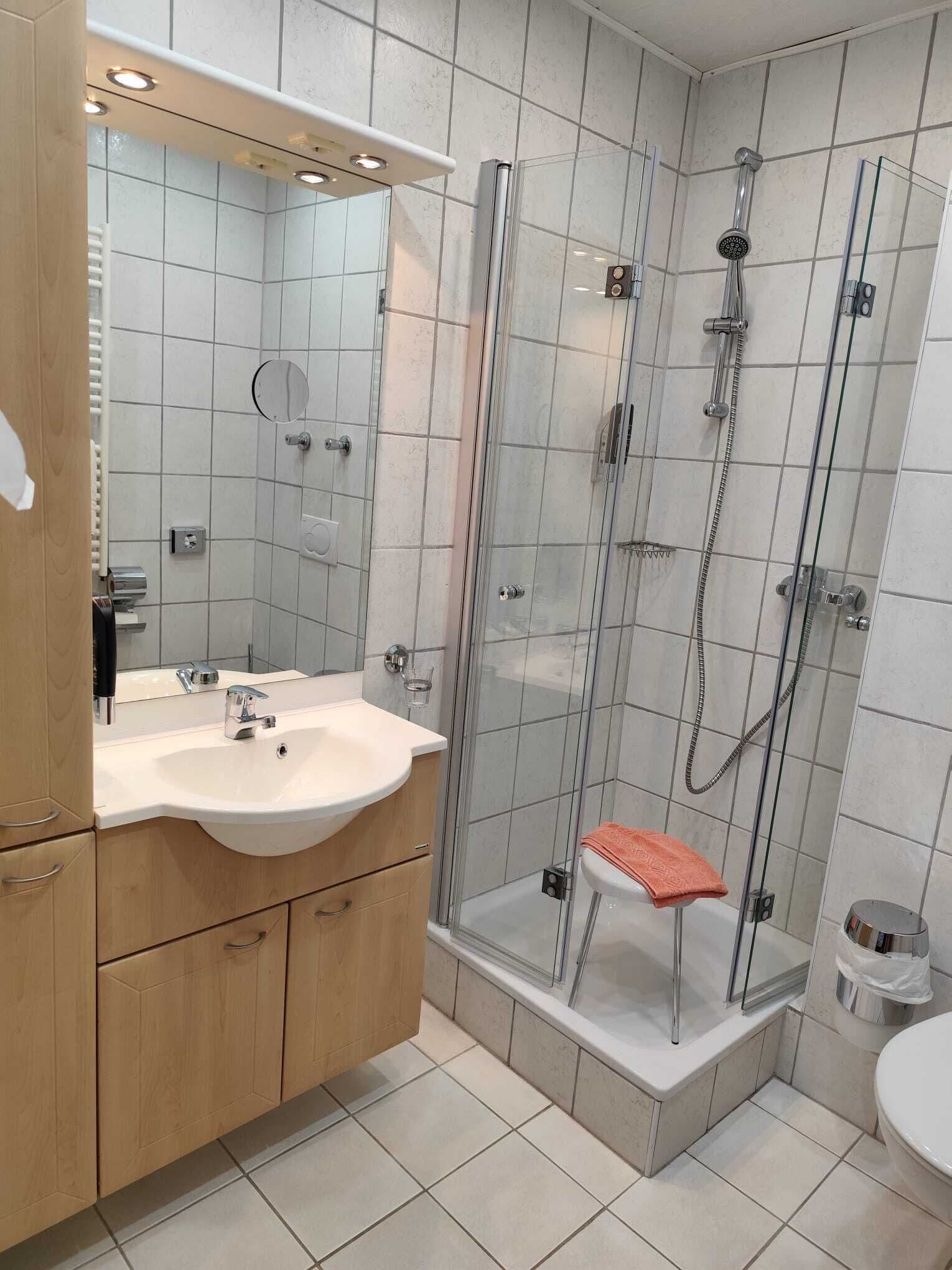 A modern bathroom with a glass-enclosed shower, a sink with a mirror, and wooden cabinets.