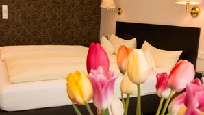 A hotel room with a neatly made bed, two wall-mounted lamps, and a floral arrangement of tulips. - Garni Hotel & Ferienwohnungen Seeschlößchen (Waldeck)
