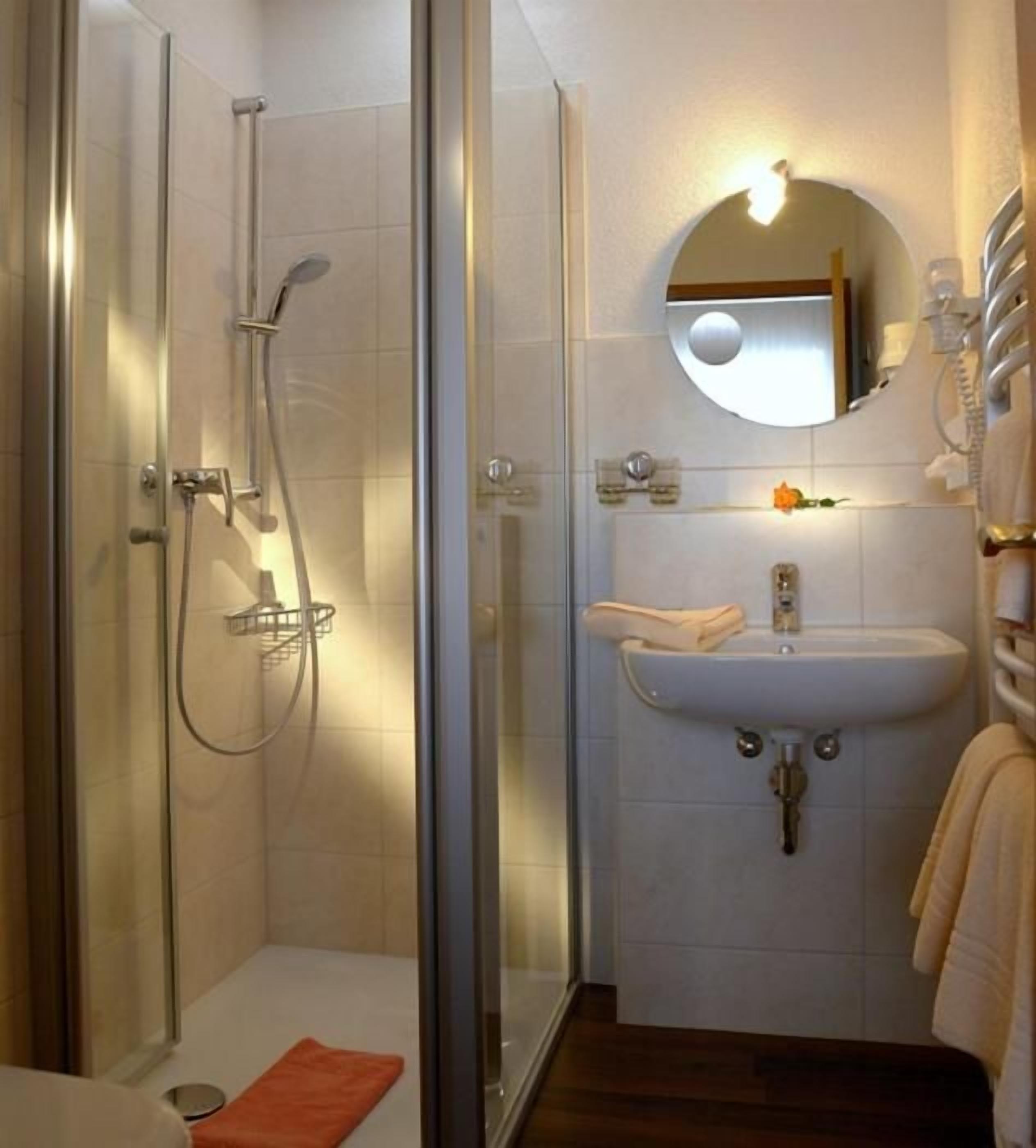 Un baño moderno con cabina de ducha de vidrio, un lavamanos con espejo y un perchero para toallas.