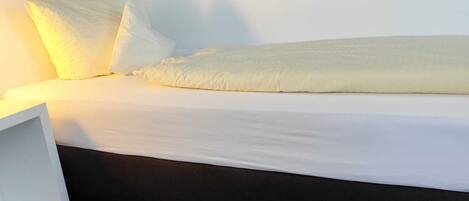 A bed with white linens, a bedside table, and a patterned wall.