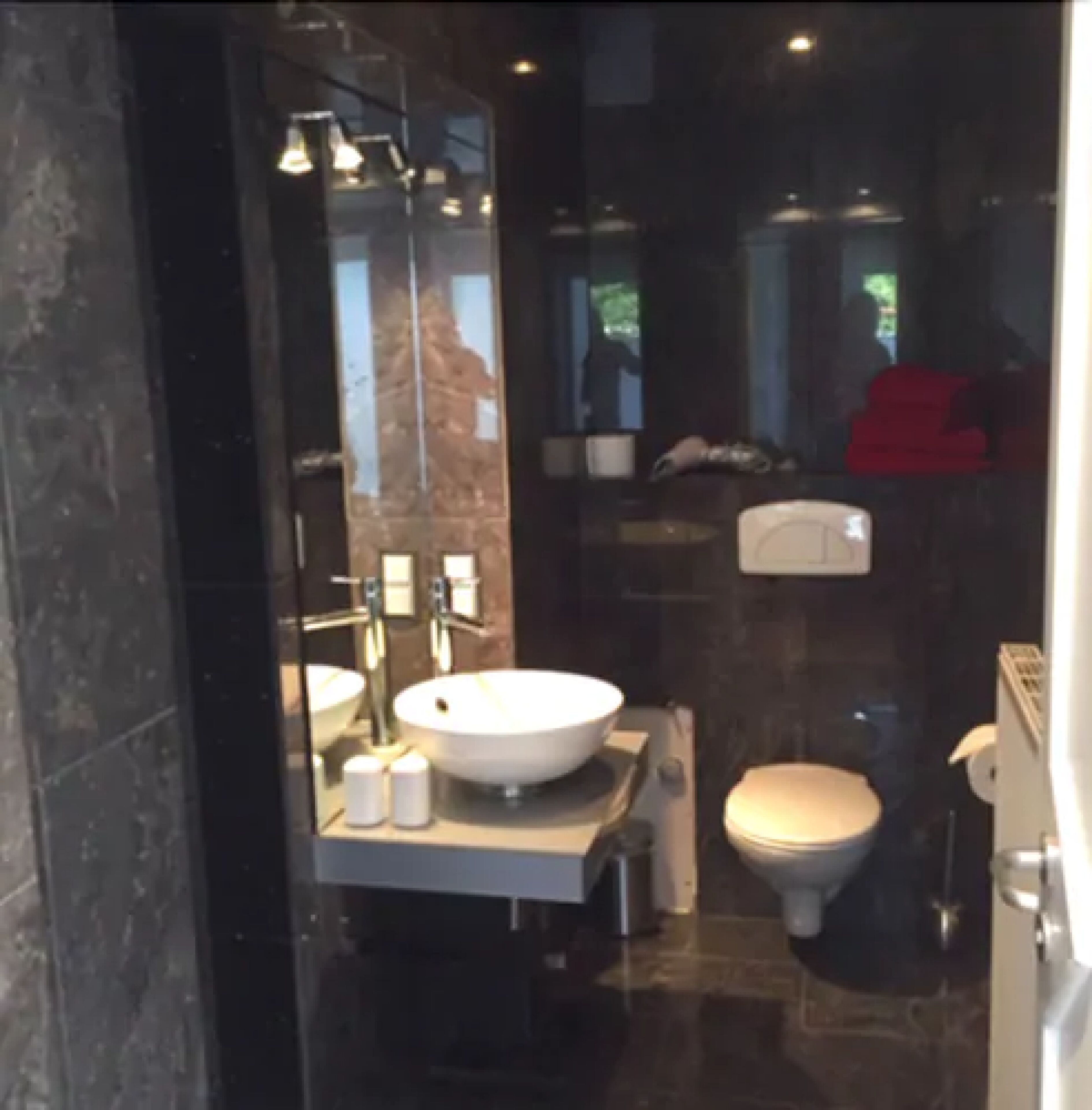 A modern bathroom with a large mirror, a white sink, and a toilet.