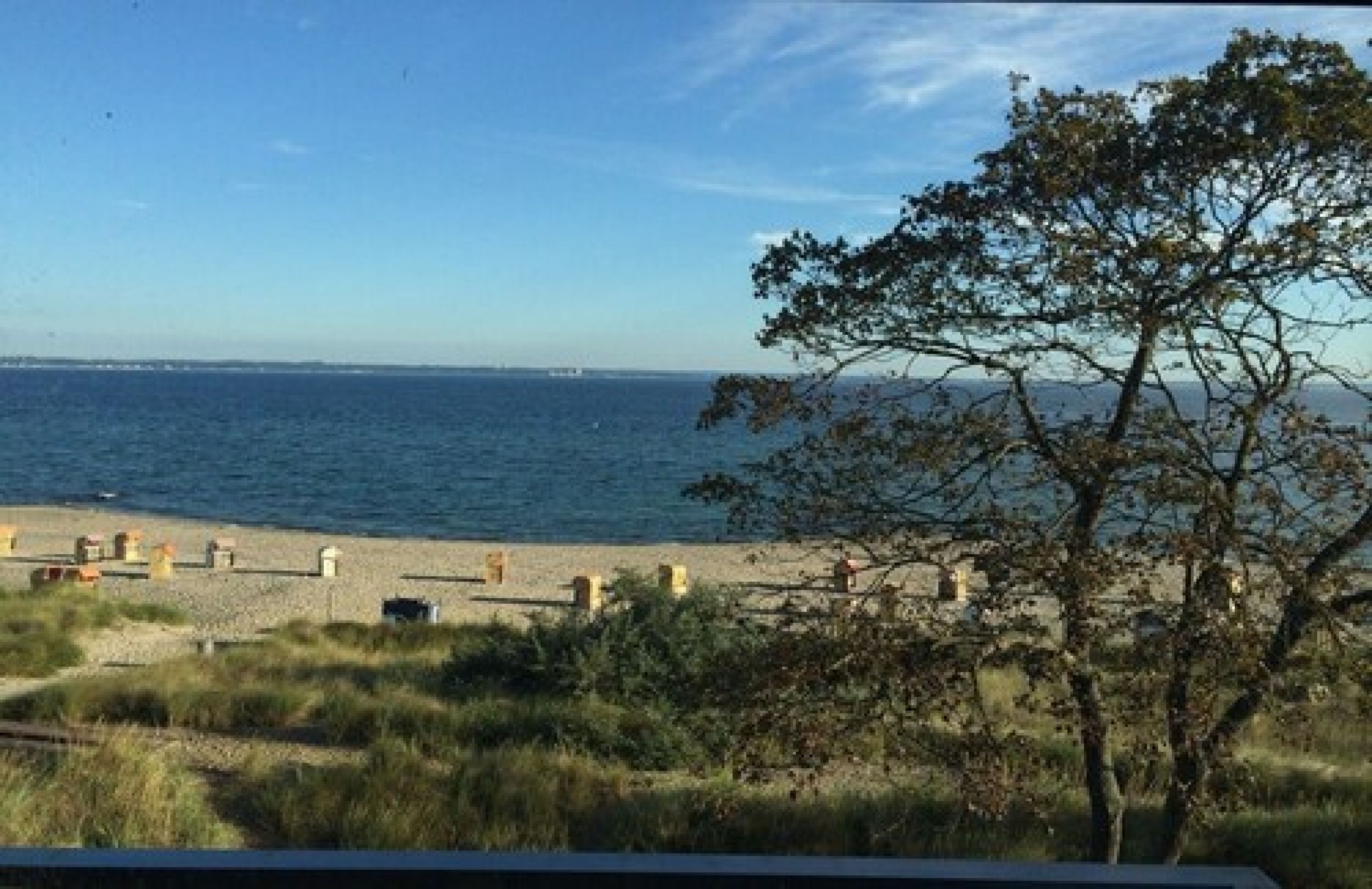 A beach with a clear view of the sea and distant land. There are some structures on the beach, possibly for beachgoers.