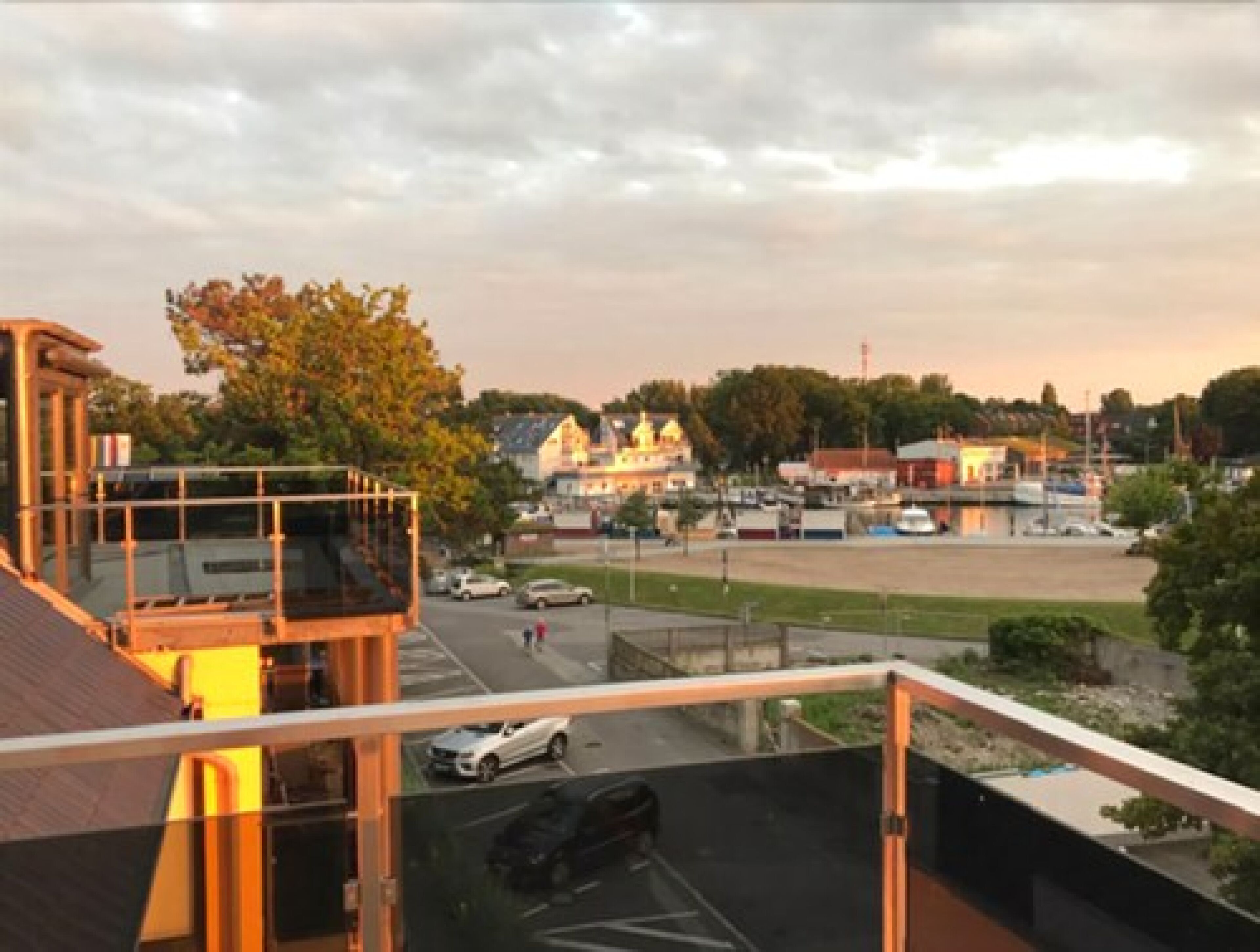 A view from a balcony overlooking a parking area with a building in the background.