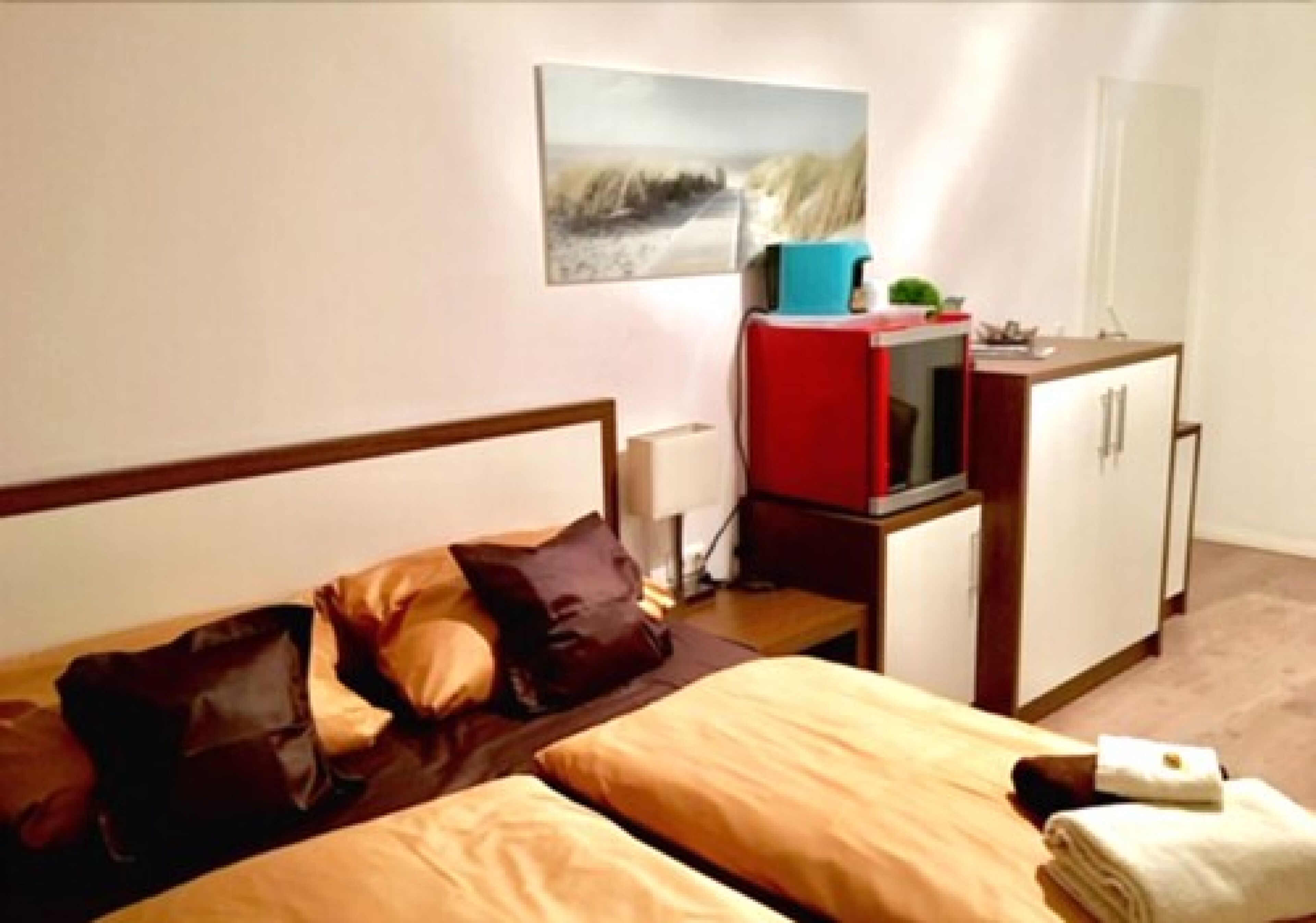 A hotel room with a bed, a desk with a computer, a cabinet, and a painting on the wall.