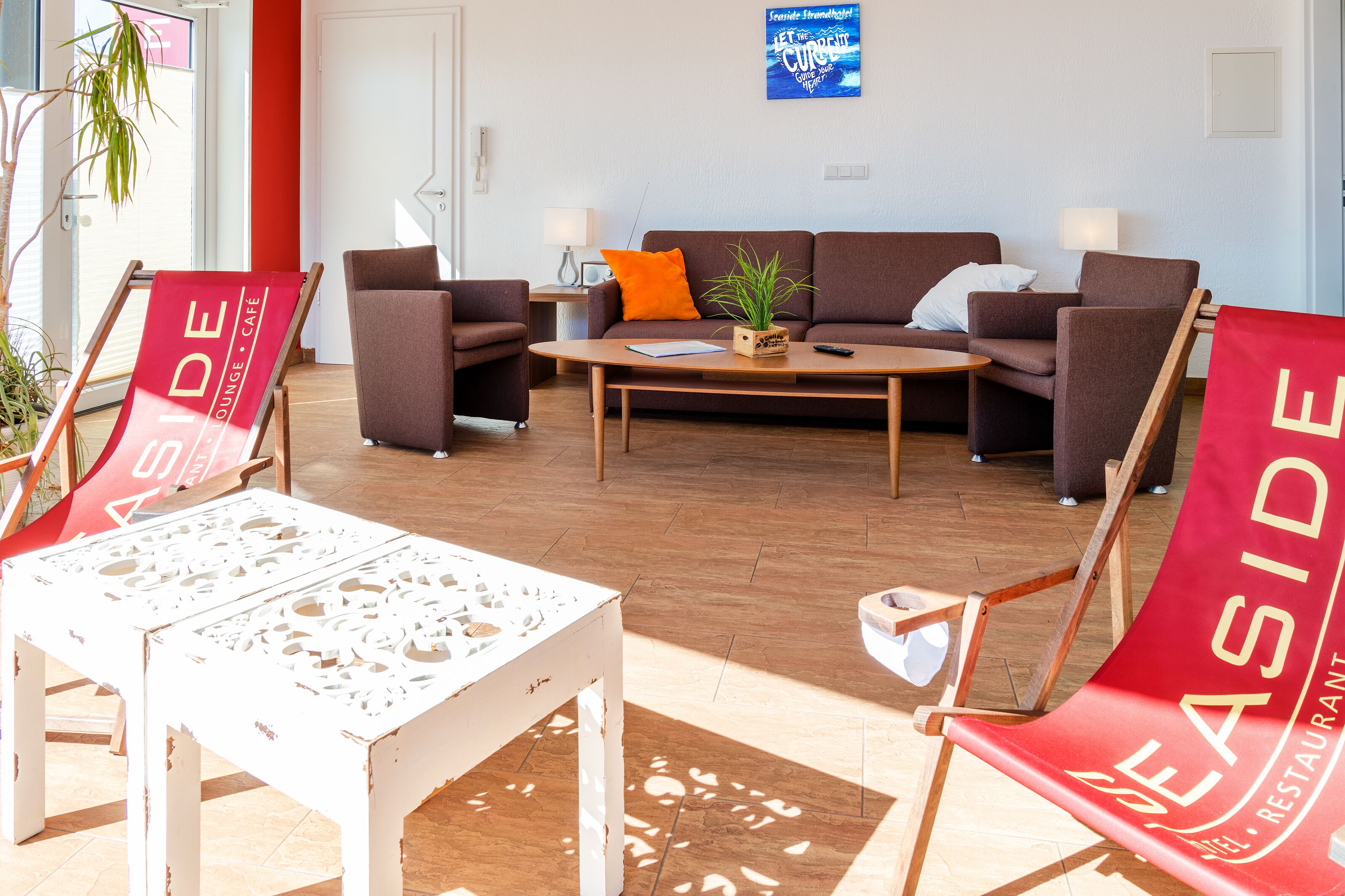 Un área de estar moderna con un sofá marrón, sillones rojos y blancos, una mesa de centro de madera y una planta en maceta.