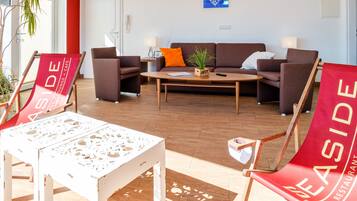 Un área de estar moderna con un sofá marrón, sillones rojos y blancos, una mesa de centro de madera y una planta en maceta.