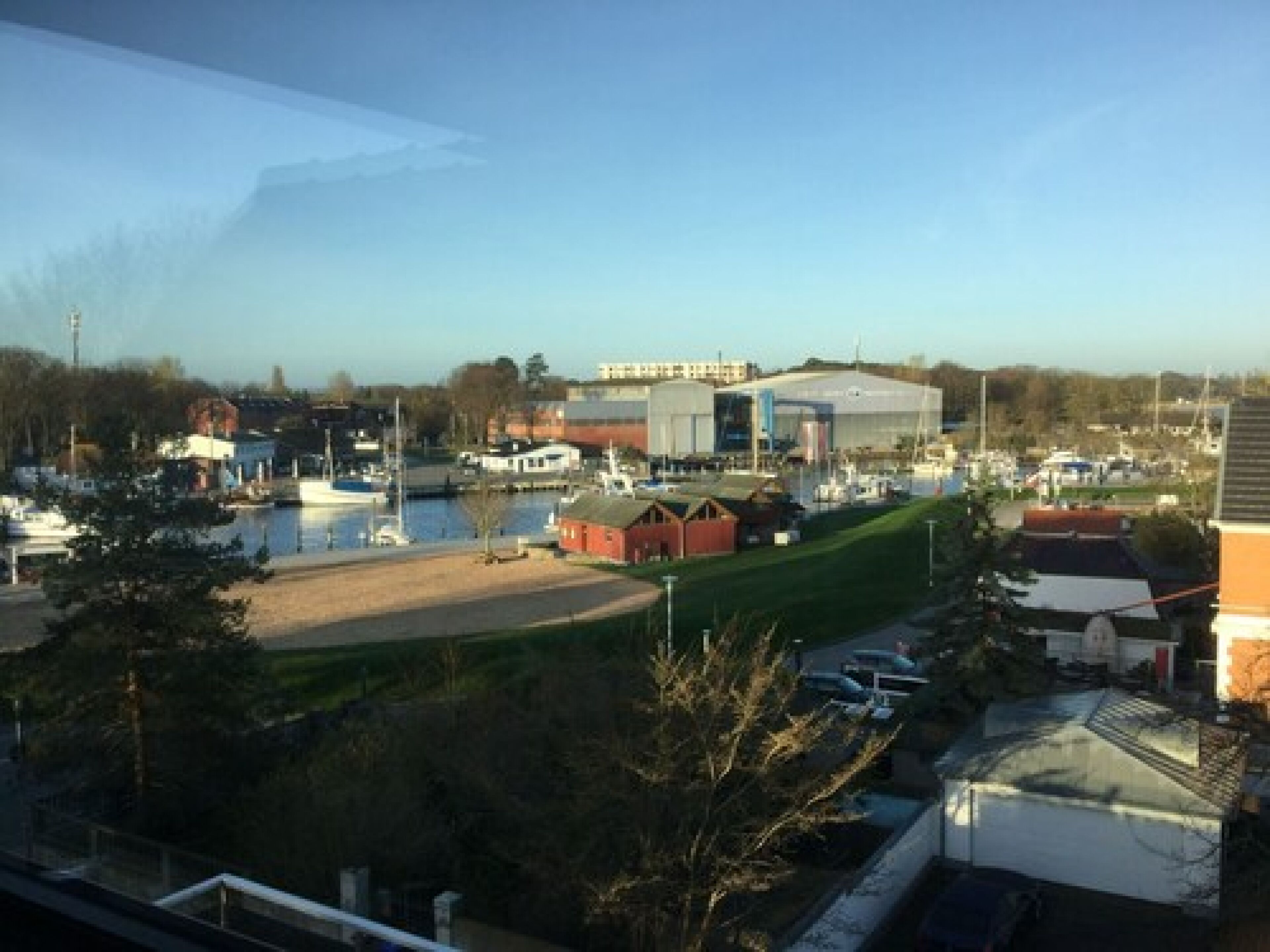 A marina with boats, a large industrial building, and a grassy area.