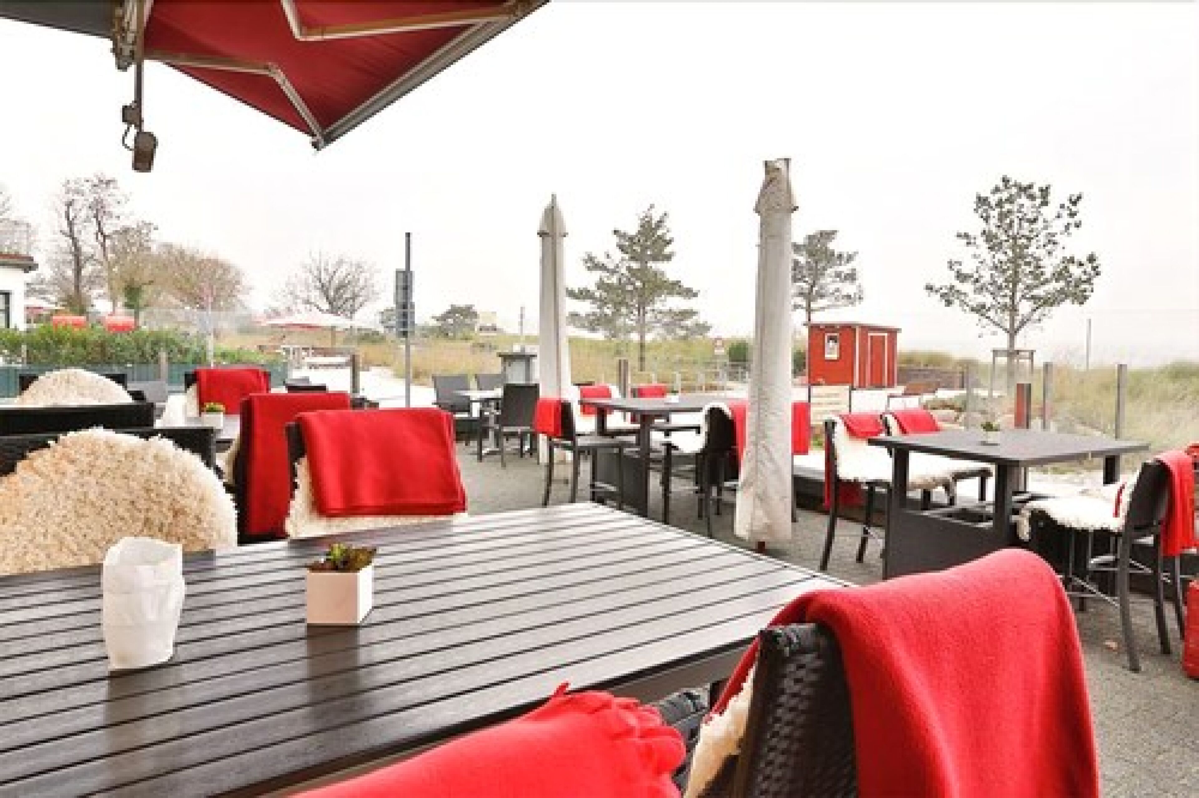 Un área de comedor al aire libre con mesas y sillas, algunas con cojines rojos.
