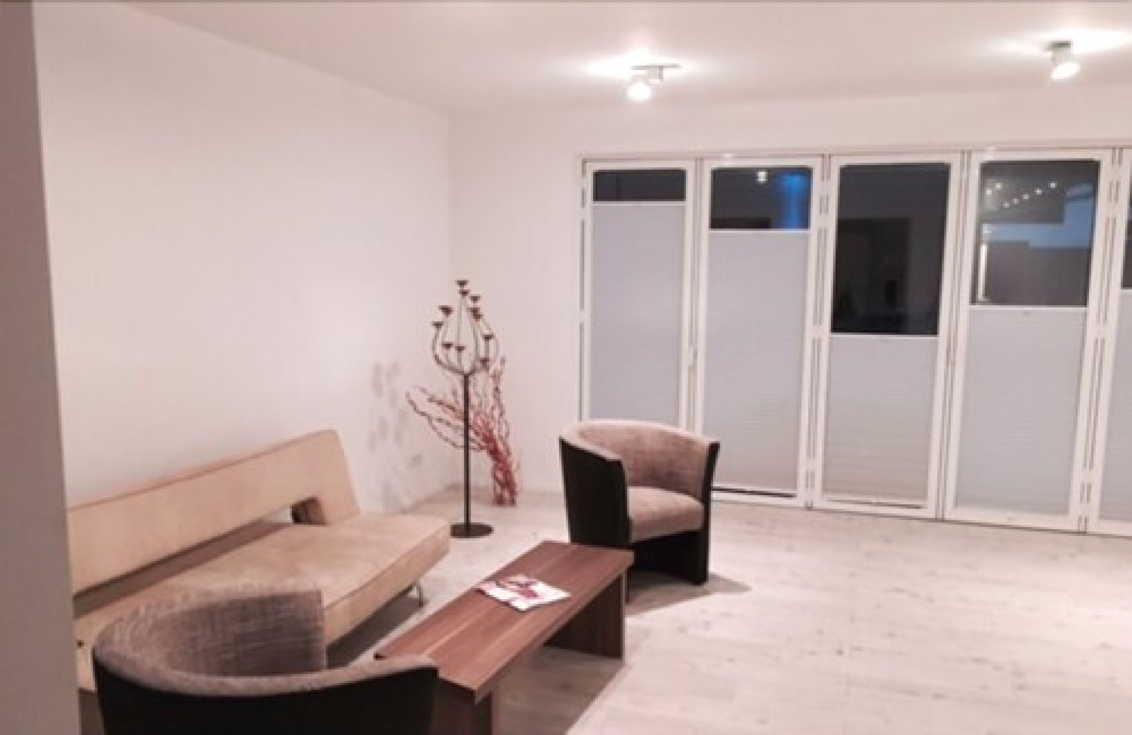 A modern room with a wooden bench, a cushioned chair, a small table, and a floor lamp.