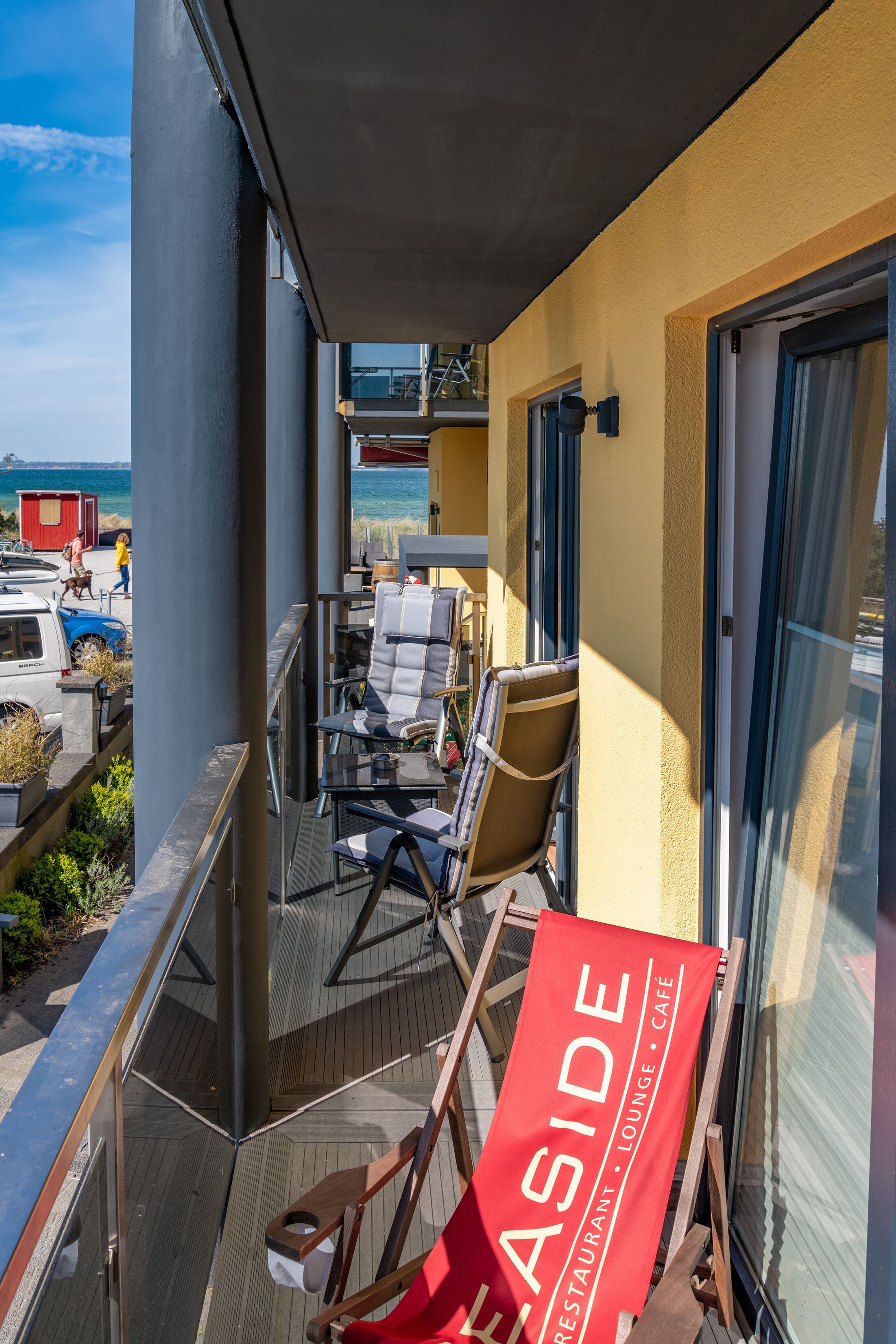 Un balcon orné d’une banderole rouge, doté de portes vitrées et offrant une vue sur la mer.