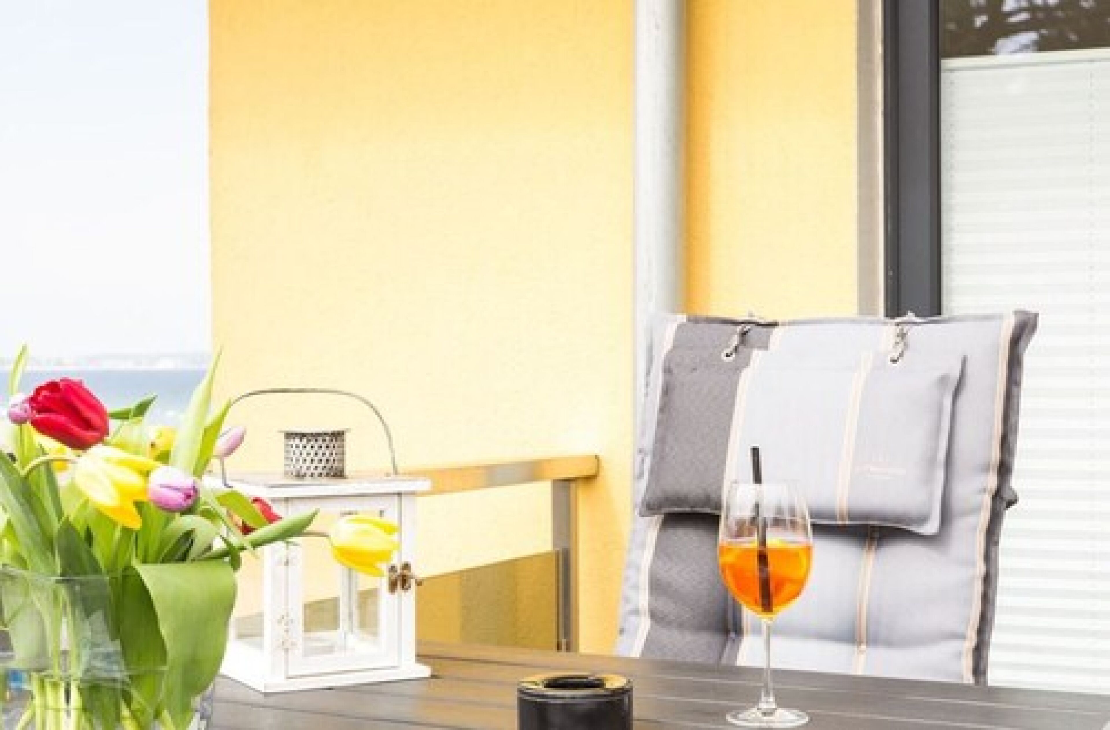 Ein Tisch mit einem Orangensaftglas, einer Tulpenvase und einer weißen Laterne.