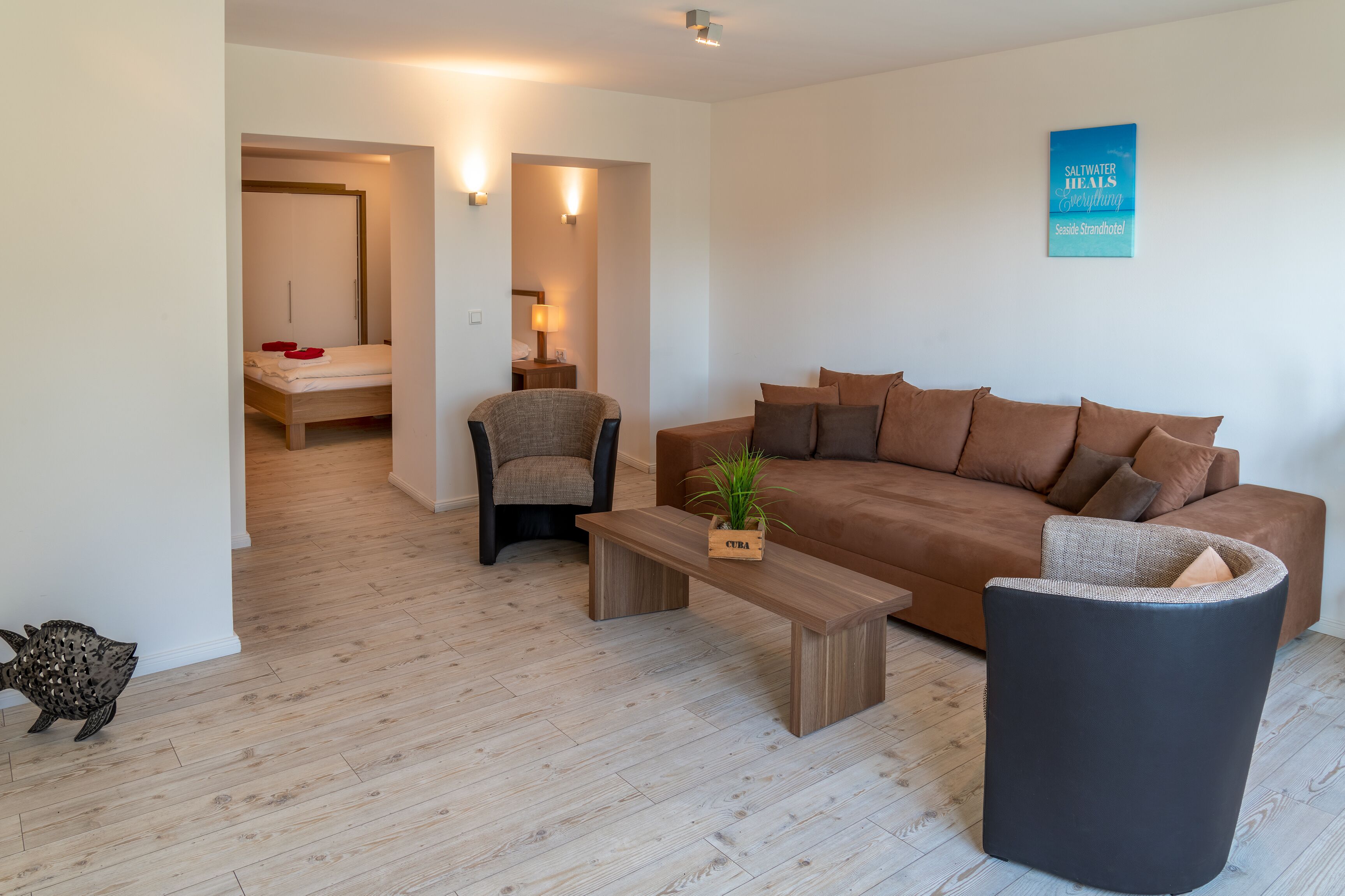 Una sala de estar moderna con piso de madera, un sofá marrón, un sillón negro, una mesa de centro de madera y una pequeña decoración de pez.