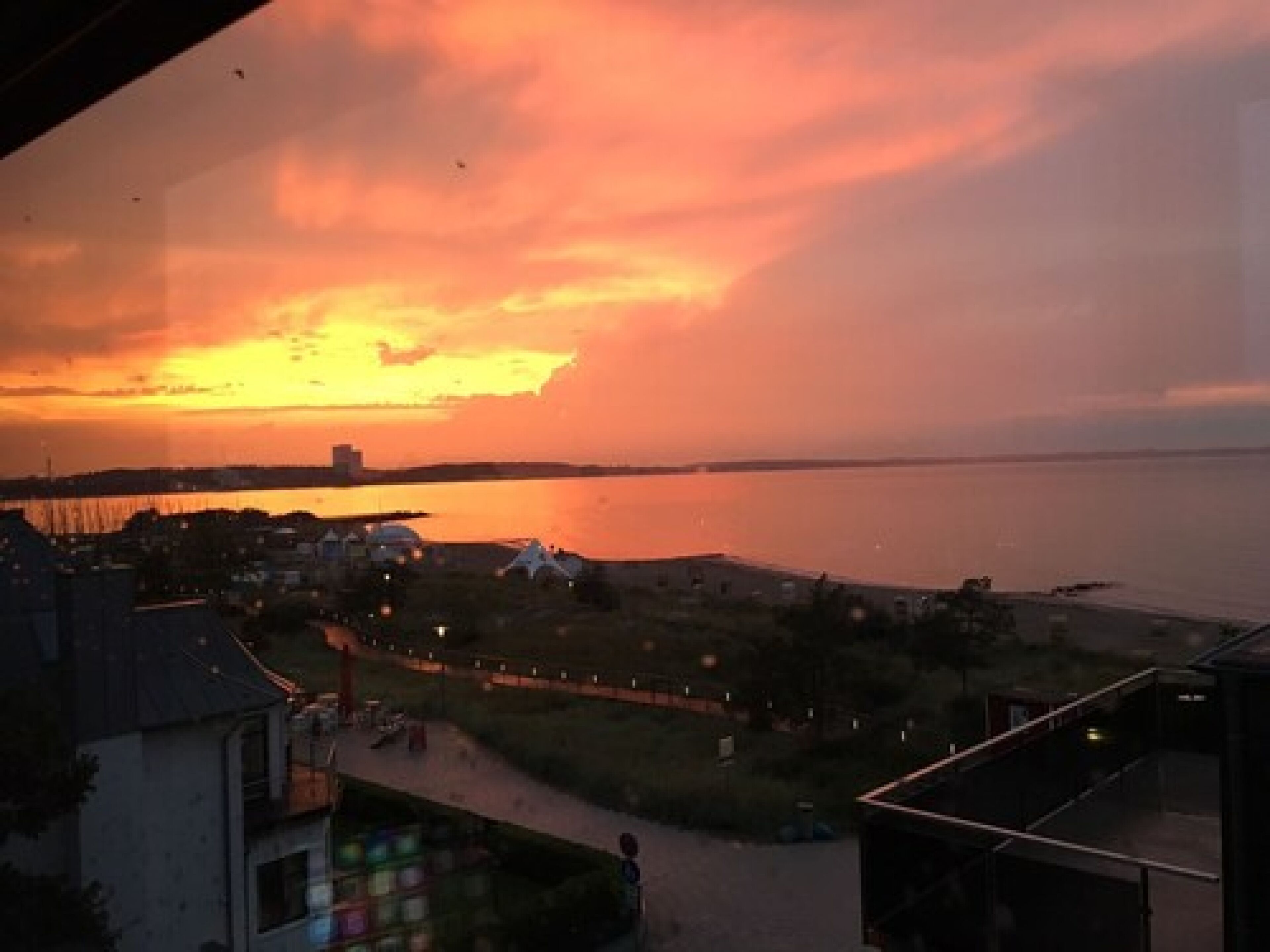 A sunset view from a window overlooking a beach with tents and a body of water.