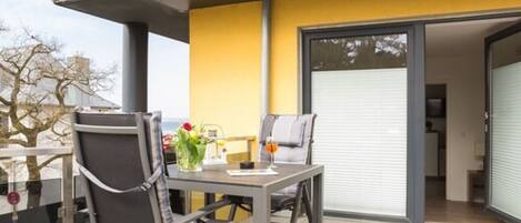 A balcony with a table, chairs, and a glass of drink.