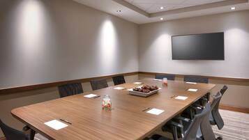 A conference room with a long table, chairs, a projector screen, and a small decorative item on the table.