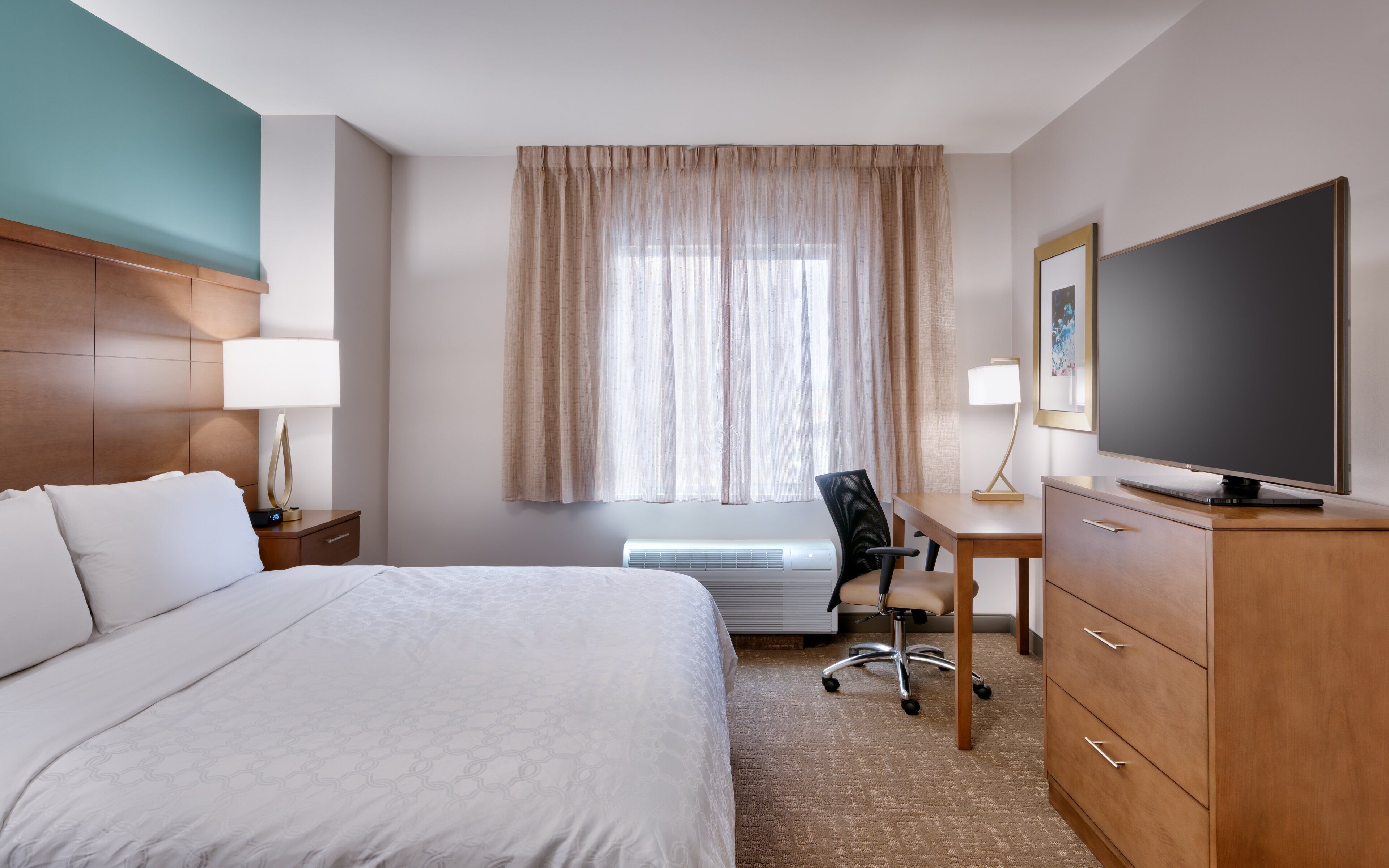 A hotel room with a bed, desk, chair, television, and a window with curtains.