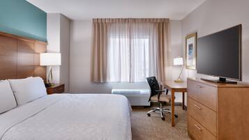 A hotel room with a bed, desk, chair, television, and a window with curtains.
