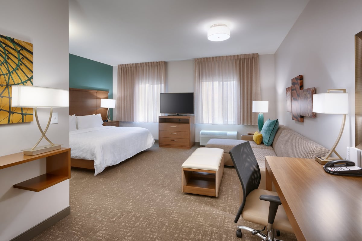 Hotellihuone, jossa on sänky, kirjoituspöytä, puhelin, tuoli, televisio ja lämmitin.