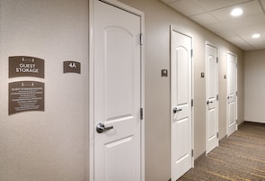 A hotel corridor with white doors, each marked with a number and a sign indicating guest storage rooms.
