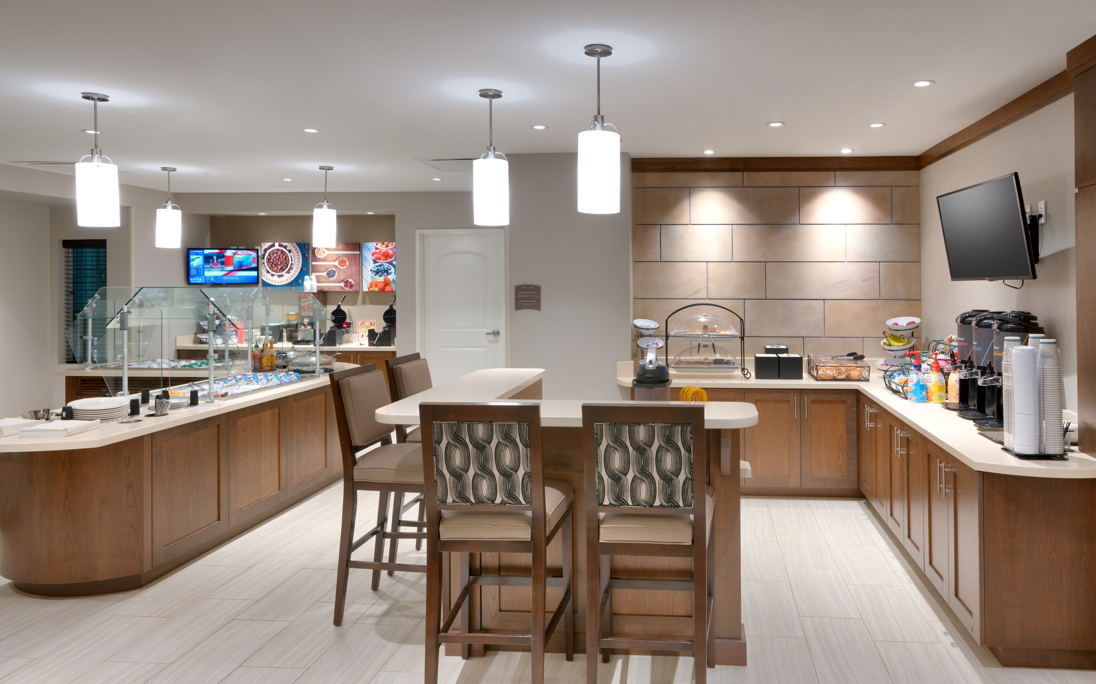 Uma cozinha moderna com ilha central, banquetas, televisão e espaço para buffet.