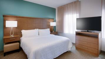 A hotel room with a large bed, two bedside tables with lamps, a TV on a wooden stand, and a window with curtains.