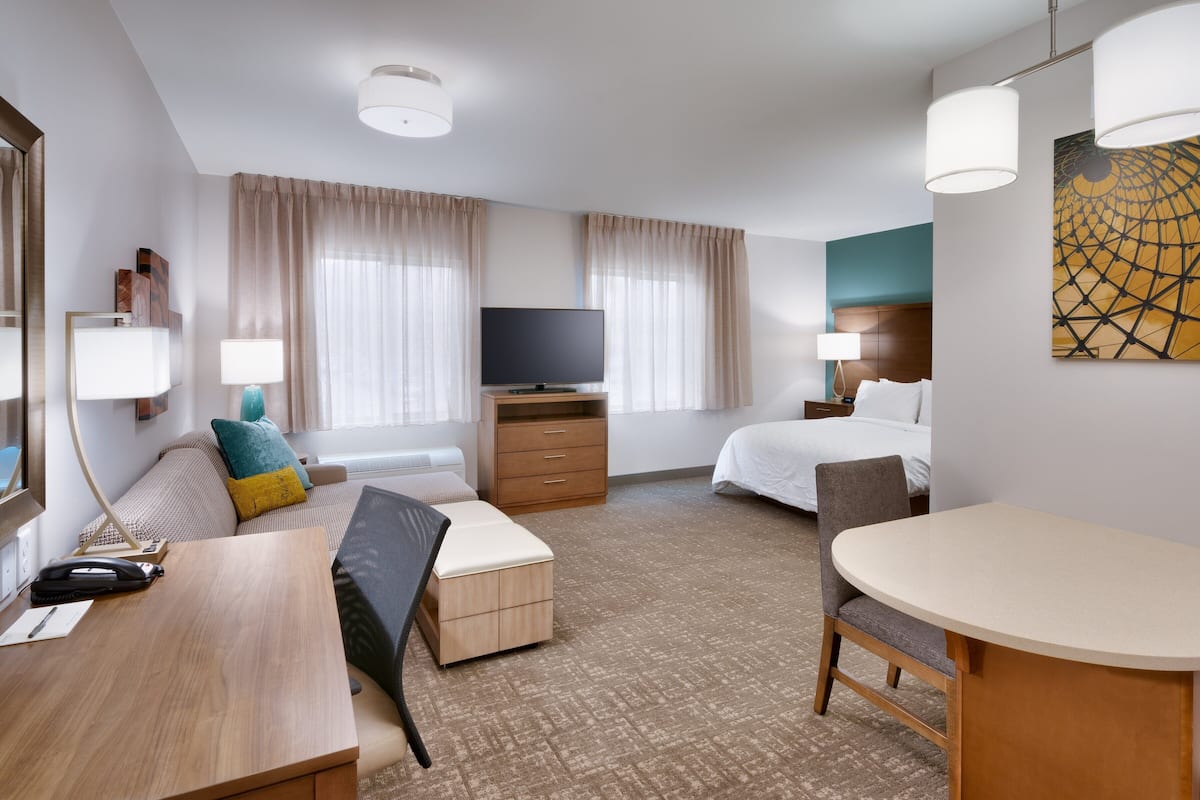 Moderni hotellihuone, jossa on sänky, työpöytä, tuoli, televisio ja taideteos seinällä.