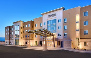 Un hotel de varios pisos con entrada cubierta, ventanas amplias y un letrero que dice 'Staybridge Suites'.