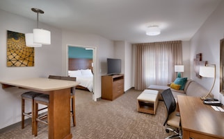 A hotel room with a bed, a TV, a desk with a chair, a sofa, and a small table.