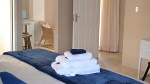 A hotel room with a bed, a stack of towels, a chair, and a desk.