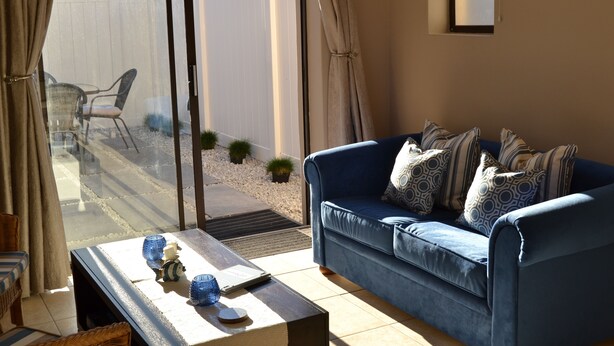 A living room with a blue sofa, a coffee table, and a view of a white fence and patio furniture.
