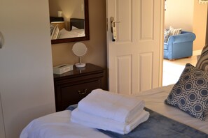 Une chambre d’hôtel avec un lit, une table de chevet avec une lampe, un miroir et un canapé bleu en arrière-plan.