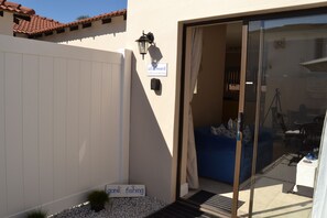 Un bâtiment moderne à l’extérieur blanc, à l’intérieur bleu, avec une porte-fenêtre coulissante donnant sur une pièce où se trouvent un canapé bleu et une table.