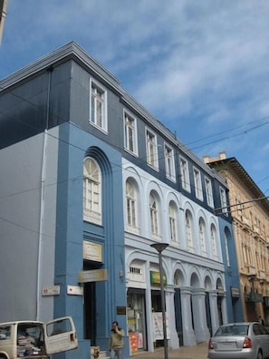 Un edificio de dos plantas con fachada azul y adornos blancos. Hay varias ventanas, algunas con arco. Una persona camina frente al edificio.