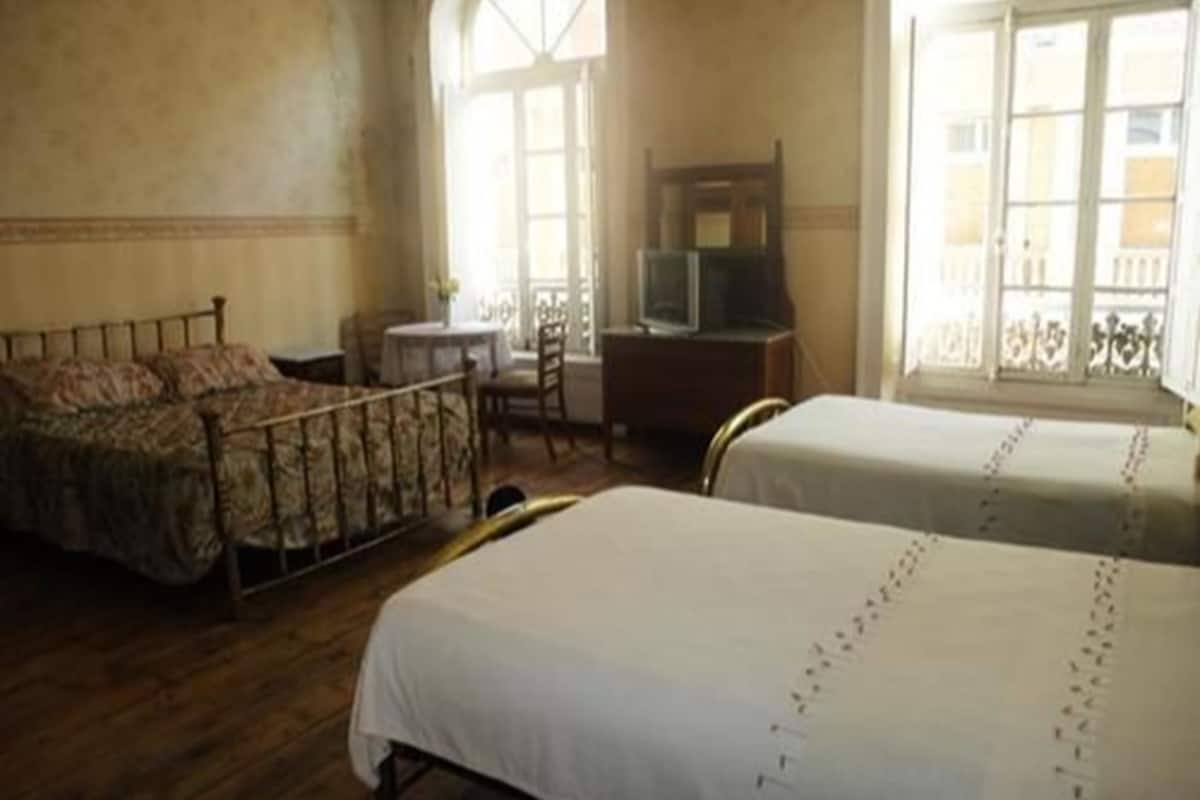 A room with two beds, a small table, a TV, and a balcony with a railing.