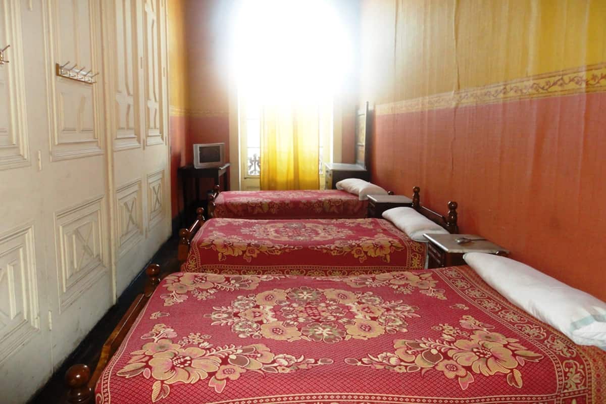 A hotel room with two beds, a television on a small table, and a view of the street through a window.