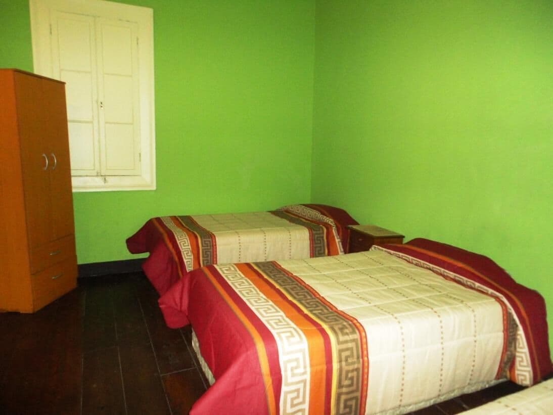 A room with two beds, a wooden wardrobe, and a window with white shutters.