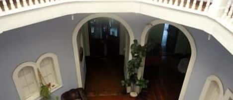 A spacious interior with a high ceiling, a balcony with white railings, and a central open area with a wooden floor.
