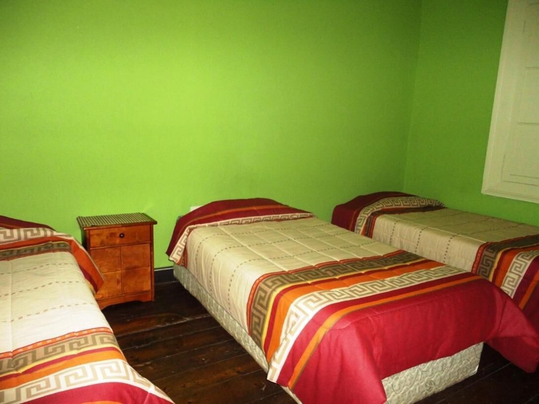 A room with three beds, each with patterned bedding and a wooden nightstand.