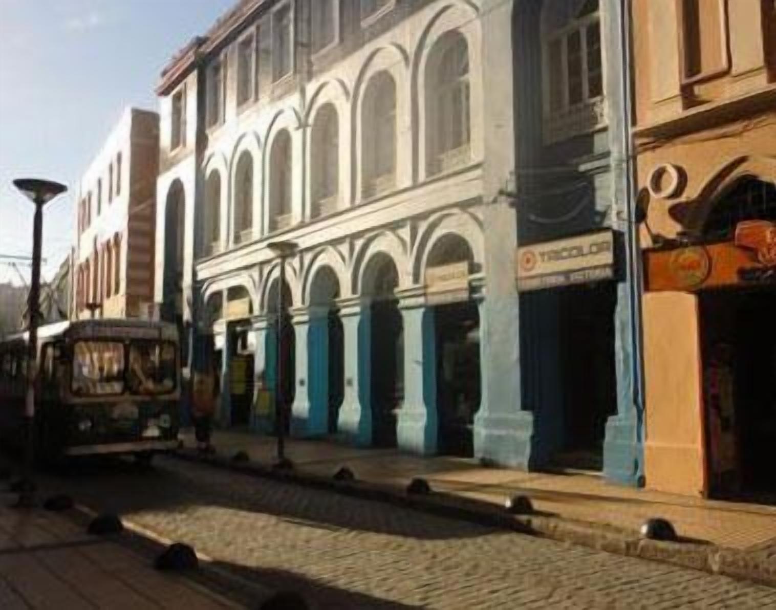 Una calle con tranvía, edificios con ventanales de arco y una tienda con cartel.