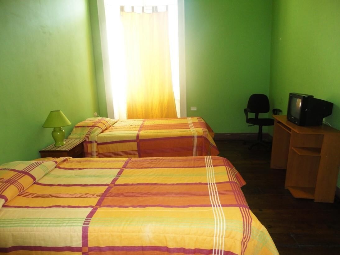 Una habitación con dos camas, un escritorio con televisor y una silla.