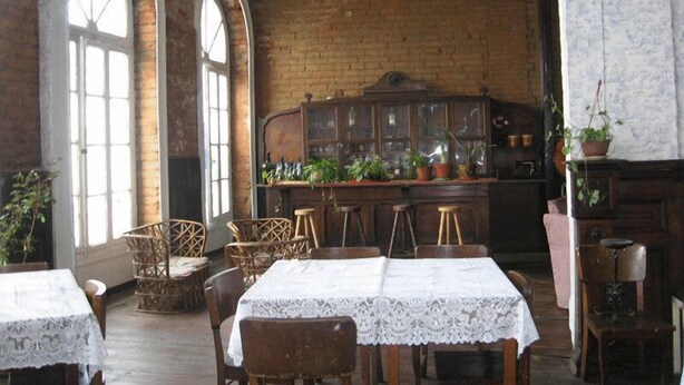 A dining area with wooden tables and chairs, a brick wall, and a cabinet with plants. - Hotel Garden (Valparaiso)